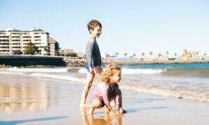 Two children playing on a sandy beach at the water's edge