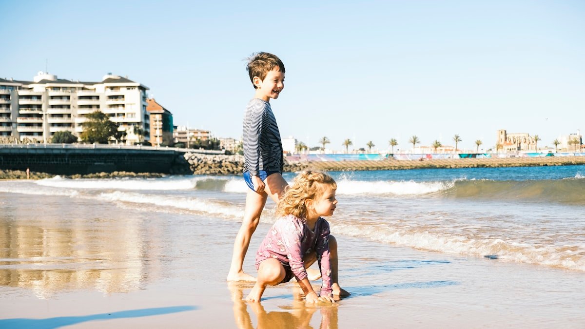Two children playing on a sandy beach at the water's edge