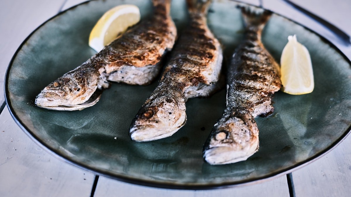 Whole grilled fish plated on a black round plate with lemon wedges